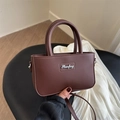Brown leather square handbag with top handle and metal logo in a hand-held display - Brown