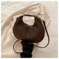 Primer plano del bolso media luna marrón oscuro con textura trenzada sobre blazer blanco - café
