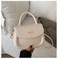 Close-up of a cream saddle handbag featuring a gold logo and soft faux leather texture - White