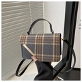 Close-up of retro plaid patchwork handbag with gold metal bar detail and leather handle - Black