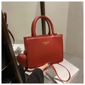 Detalle del bolso de mano rojo en cuero con logo dorado, mini estuche y correa ajustable - Rojo