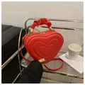 Detail of red heart-shaped bag with quilted texture and ruched handle on display - Red