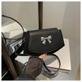 Detail of a black crossbody bag showing the silver metal bow buckle and PU leather texture - Black