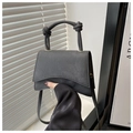 Detail of black minimalist handbag featuring a wavy bottom and knotted handle design - Black