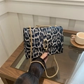 Borsa a tracolla leopardata con catena dorata e texture morbida su un tavolo di vetro - Nero