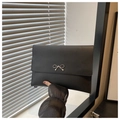 Detail shot of a black envelope clutch featuring a decorative silver metal bow clasp - Black