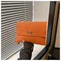 Macro shot of orange envelope clutch with silver metal bow and fine stitching detail - Orange