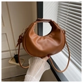 Detailed view of a caramel moon shaped handbag held against a soft window light - Brown