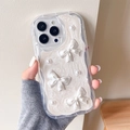 Detail der gewellten iPhone-Hülle mit cremiger Textur, Schleife und Perlenbesatz - Cremefarbene Hülle Weißer Glitzer Tropfkleber Perlmuttschleife / iPhone 7/8/SE 2020