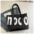Vista piatta di una grande borsa tote noco nera su jeans con un'atmosfera lifestyle sobria - Stile con Grande Stampa di Lettere (noco) / Nero