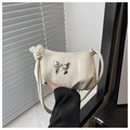 Macro detail of cream white handbag featuring a silver mirror bow and pearl bead strap knots - White