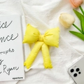 Detail of a soft yellow fabric bow phone grip holder on a minimalist fabric background - Transparent Stand - Plush Bow / Yellow