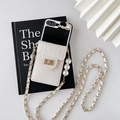 Detail of white quilted phone case with gold lock, pearl charms and chain strap - White / Samsung ZFlip3
