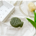 Close-up of olive green fish-shaped phone grip on white fabric with elegant accessories - Green