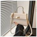 Close-up of cream crocodile pattern handbag with golden twist lock and top handle - White