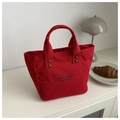 Detail der roten Canvas-Handtasche mit schwarzem Schriftzug und Metallnieten-Verstärkung - Rot