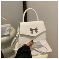 Detail of white leather crossbody bag with silver bow buckle on white pedestal - White