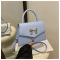 Close-up of light blue leather handbag featuring a gold bow buckle and crossbody strap - Blue