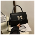 Close-up of black leather handbag featuring a polished silver bow clasp and top handle - Black
