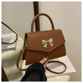 Detail of a brown crossbody bag with a golden bow buckle and adjustable strap - Brown