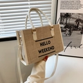 Straw tote bag with white leather straps and Hello Weekend print in a soft room setting - Off White