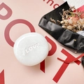 Close-up of white pebble-shaped phone grip with Love engraving on a pink background - Marble White (Love)