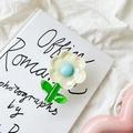 Détail du support de téléphone floral avec pétales et cœur bleu sur un livre blanc - Fleur à Feuilles Vertes en Cristal / Jaune