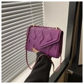 Detail einer lila gesteppten Handtasche mit goldener Kette und Wellenstruktur - Lila