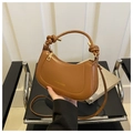 Detail of caramel crescent bag with knot handle and gold hardware on a leather surface - Brown