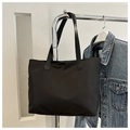 Detalle del bolso tote de nailon negro con asas reforzadas colgado en una percha - Negro