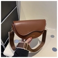 Close-up of brown leather saddle bag with wide shoulder strap and gold metallic hardware - Tan