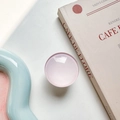 Detailed view of a pink translucent round phone grip on a vintage book and blue tray - White Base Stand / Light Pink