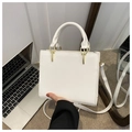 Detail view of white leather handbag with gold metal hardware and stitching accents - White