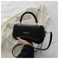 Close-up of black leather curved handbag with gold fashion lettering and handle detail - Black