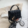 Black quilted crossbody bag with gold buckle and top handle in a lifestyle setting - Black