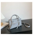 Detailed view of light grey top handle bag with front zipper pocket on a minimalist table - Gray
