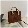 Dettaglio di una borsa marrone con motivo a coccodrillo e foulard in seta sul manico - caffè