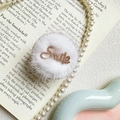 Dettaglio macro del supporto per telefono in peluche con scritta Smile in strass e perle - Bordo Dorato Tondo