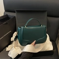 Borsa a mano verde scuro con chiusura dorata e tracolla avorio su sfondo di seta morbida - Verde