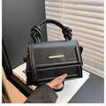 Strukturierte schwarze Handtasche mit Knotengriff und goldener Hardware auf weißem Buch - Schwarz