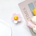 Detailed view of a pink floral phone grip with a yellow smiley face on a bright desk - Pink