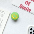 Detail of expandable green phone grip with 3D yellow smiley face on desk - Green
