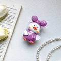 Dettaglio del supporto per telefono a forma di papera viola 3D su un libro - Stile Anatra con Fiocco Viola