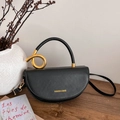 Elegant black crescent saddle bag with gold twisted metal handle on a wooden table - Black