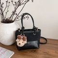 Vintage-Beuteltasche aus schwarzem Leder-Mix mit Teddybär-Anhänger auf einem Holztisch - Mit Anhänger / Schwarz