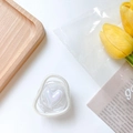 Détail d'un support de téléphone en acrylique avec un cœur en perle irisée sur fond floral - Forme de Cœur de Travers