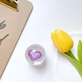 Detail shot of a crystal phone grip with a purple heart on a clean aesthetic desk - Purple