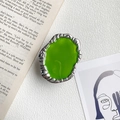 Dettaglio del supporto per cellulare in metallo argento con resina verde su un libro - Ovale Lineare / Bordo Argento Verde