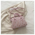 Detalle de mini bolso rosa con estampado de cerezas sobre blazer beige y luz natural - Rosa
