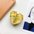Macro detail of heart-shaped phone grip with yellow resin and colorful sequins - Yellow
